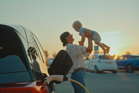 Frau spielt mit Baby neben einem ladendem Elektroauto