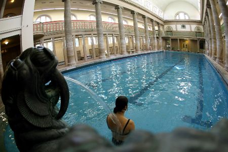 Frau lässt sich im Becken des Stadtbads Neukölln von einem antiken Wasserspeier bespritzen