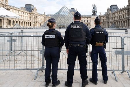 Drei Polizisten stehen vor der Pyramide des Louvre