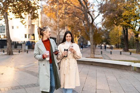 Zwei junge Frauen gehen im Herbst in der Stadt spazieren.