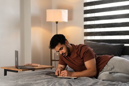 Junger Mann liegt auf einem Bett und schreibt in ein Tagebuch