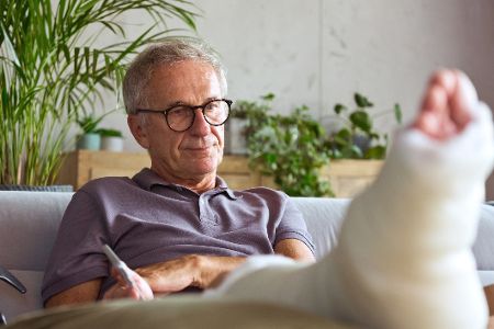 Älterer Mann sitzt auf dem Sofa mit einem bandagierten Fuß