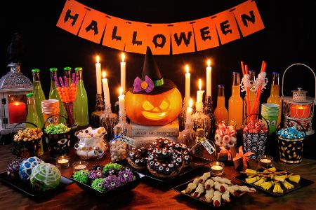Tisch dekoriert mit einem Halloween-Schild und verschiedenen gruseligen Speisen und Drinks in passender Optik
