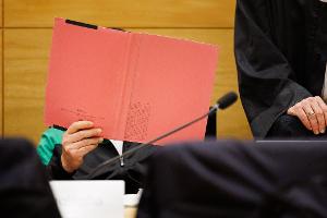 Einer der Angeklagten am Landgericht Bielefeld sitzt neben seinem Verteidiger und verdeckt sein Gesicht.