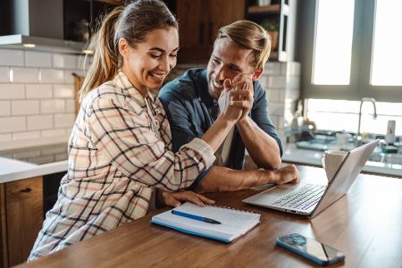 Junge Frau und junger Mann sitzen zuhause vor dem Laptop und geben sich High Five