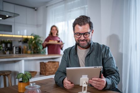 Frau bringt dem Mann etwas zu essen, während er am Laptop arbeitet