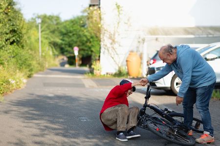 Mann hilft einem Kind auf, das mit dem Fahrrade gestürzt ist