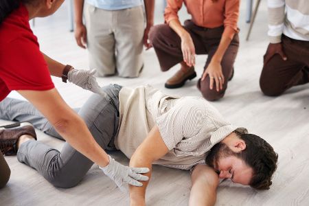 Eine Person liegt in der Mitte in der stabilen Seitenlage, andere sitzen herum und schauen zu