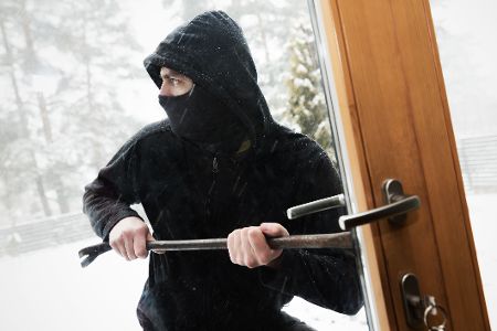 Maskierter Einbrecher hebelt im Winter eine Tür auf