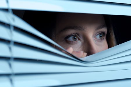 Frau schaut ängstlich durch eine Jalousie