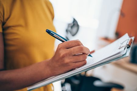 Frau schreibt auf einer Liste auf einem Klemmbrett Dinge auf