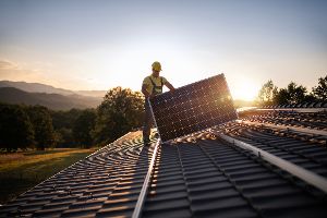 ein Arbeiter hantiert bei Sonnenuntergang mit einem Solarpanel auf einem Hausdach