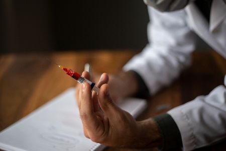 Mensch in Arztkittel hält aufgezogene Spritze in der Hand