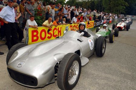 Rennfahrer sitzt vor einer Menschenmenge in einem Oldtimer-Sportrennwagen