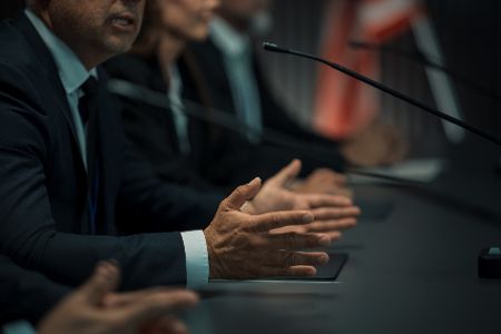 Männer und Frauen in Anzügen sitzen und Mikrofonen und verhandeln