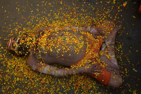 Bei einem hinduistischen Frühlingsfest in Indien liegt ein Sadhu mit Blütenblättern bedeckt auf der Straße. 