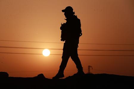 Ein Mitglied der Popular Mobilization Forces läuft an einer Betonmauer entlang.