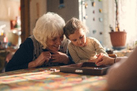 Großmutter spielt mit Enkel ein Spiel an einem Tisch