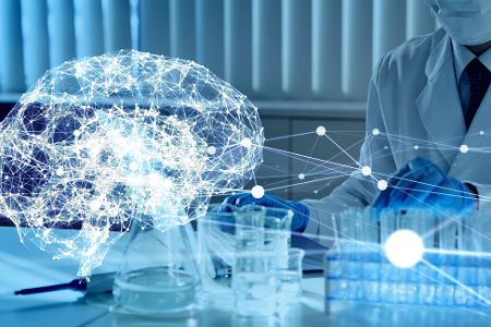 Mensch im Kittel sitzt vor einem Rechner, vor ihm ein digitales Gehirn