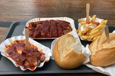 Zwei Schalen mit Currywurst, eine mit Pommes und zwei Brötchen auf einem Tisch