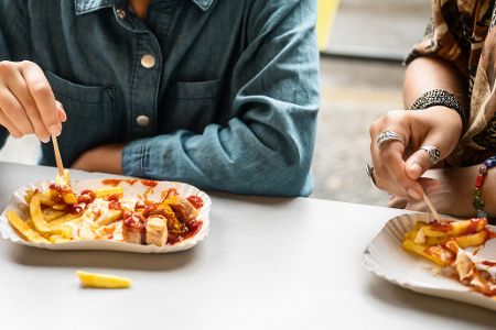 Zwei Menschen sitzen in einem Imbiss und essen Currywurst