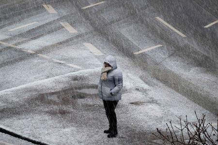 Eine Person steht bei starkem Schneefall an einer Kreuzung in Frankfurt. 