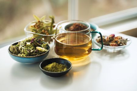 Teeglas mit Kräutertee inmitten von verschiedenen Kräutern