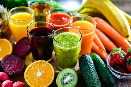 Mehrere Gläser mit buntem Fruchtsaft stehen mitten in arrangierten Früchten aller Art