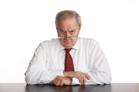 Älterer Mann in Hemd und Krawatte schaut streng über Brillenrand