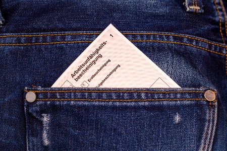 Eine Arbeitsunfähigkeitsbescheinigung schaut aus einer Hosentasche halb hervor