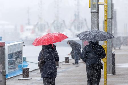 Menschen schützen sich vor Schneefall mit Regenschirmen bei einem Spaziergang an den Landungsbrücken am Hamburger Hafen.