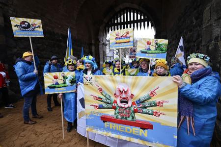 Der ukrainische Hilfsverein Blau-Gelbes-Kreuz hält Plakate mit Putin-Motiven hoch. Das ist als Zeichen der Solidarität mit Wagenbauer Jacques Tilly gemeint. Dieser wird in Russland strafrechtlich verfolgt. 