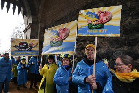 Mitglieder des ukrainischen Hilfsvereins Blau-Gelbes Kreuz halten im Kölner Rosenmontagszug Plakate mit früheren Putin-Darstellungen aus den Zügen in Köln und Düsseldorf hoch.