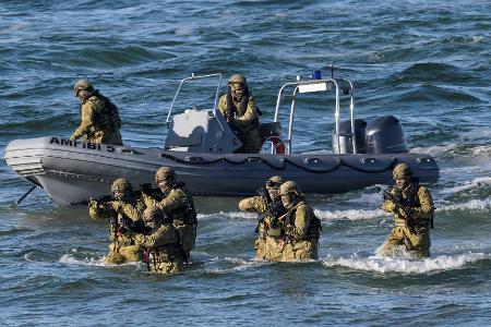 Taucher machen den Anfang und steigen aus dem Wasser auf den schneebedeckten Strand, um den Küstenabschnitt zu sichern.