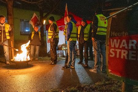 Streikende in Warnwesten wärmen sich in Augsburg an einem Feuer während eines Warnstreiks im ÖPNV.