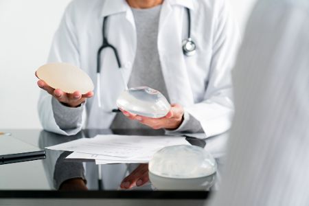 Arzt hat zwei Brustimplantate in der Hand