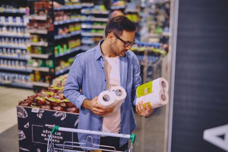 Mann im Supermarkt hat zwei Toilettenpapiertüten in der Hand und studiert ihre Aufschrift