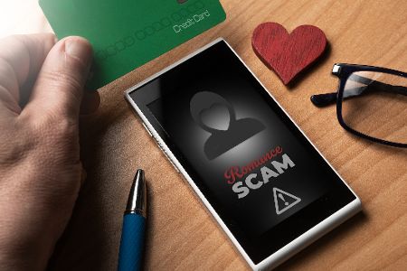 Handy liegt auf dem Tisch, daneben ein Herz, auf dem Display steht Romance Scam