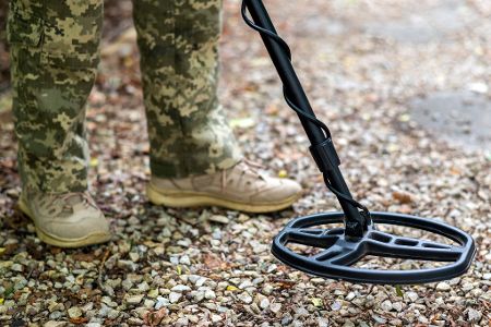 Mensch in Tarnkleidung sucht etwas mit einem Metalldetektor