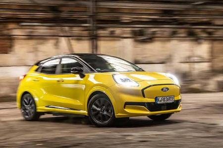 Ford Puma Gen-E Premium in gelb, fahrend in einer Halle mit eingeschaltetem Scheinwerfer, Seitenansicht.