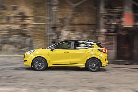 Seitenansicht eines gelben Ford Puma Gen-E Premium in Bewegung, aufgenommen in einer Industriehalle.