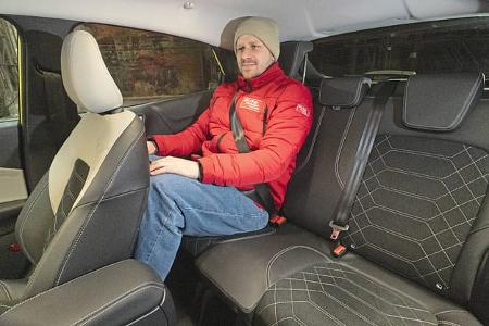 Innenaufnahme eines Ford Puma Gen-E Premium mit einer Person auf der Rückbank. Die Sitze und das Platzangebot im Fond sind deutlich zu erkennen. Die Person trägt eine rote Jacke und eine Mütze.