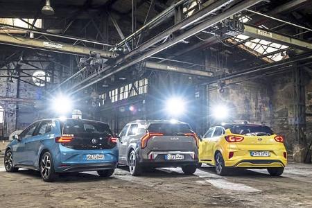 Drei Elektrofahrzeuge – Ford Puma Gen-E, Kia EV3 und VW ID.3 – stehen nebeneinander in einer alten Industriehalle, fotografiert von hinten.