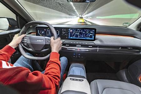 Innenraum des Kia EV3 58,3 kWh während der Fahrt, Blick auf Cockpit, Lenkrad und Infotainment-Display.