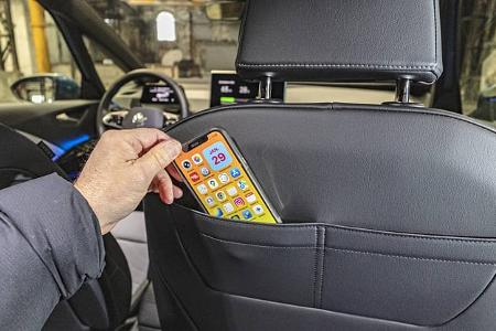 Detailaufnahme des Innenraums eines VW ID.3 52 kWh, bei der eine Hand ein Smartphone in die Rückentasche des Vordersitzes steckt. Im Hintergrund sind das Cockpit und das Lenkrad des Fahrzeugs sichtbar.