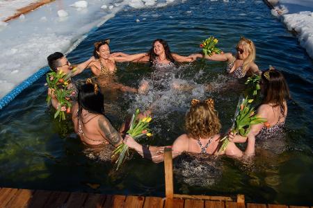 Mitglieder eines Winterschwimmclubs feiern in einem Eisloch den Internationalen Frauentag.
