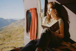Woman reading book in camper van in mountains