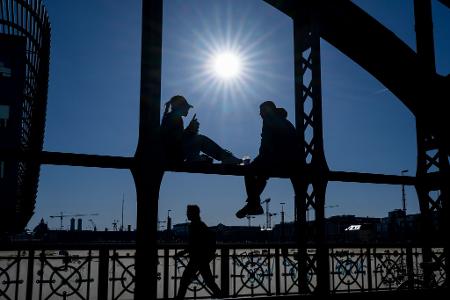 Ein Pärchen sitzt in der Sonne auf dem Geländer der Hackerbrücke in München. 