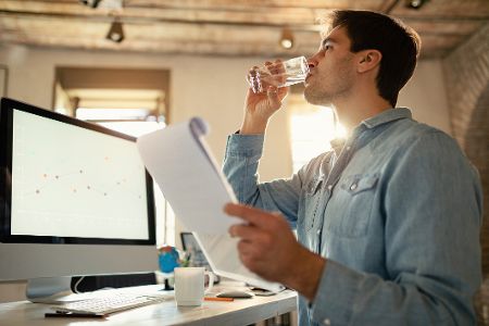 Mann am Computer im Büro trinkt ein Glas Wasser