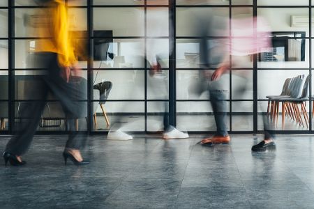 Büroflur im Zeitraffer mit Silhouetten vorbeieilender Menschen